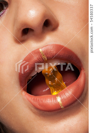 Close up view of beautiful woman lips with gummy bear 54580337