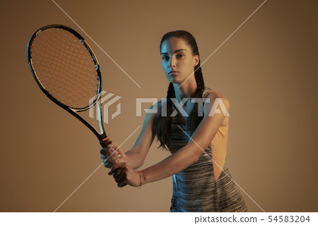 One caucasian woman playing tennis on brown background in mixed light One caucasian woman playing tennis on brown background in mixed light 54583204