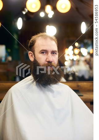Male client with beard sitting in hairdresser chair. Serious man with long brown beard. Modern Male client with beard sitting in hairdresser chair. Serious man with long brown beard. Modern 54586953