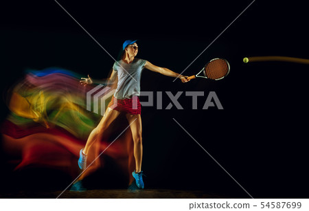 One caucasian woman playing tennis on black background in mixed light 54587699