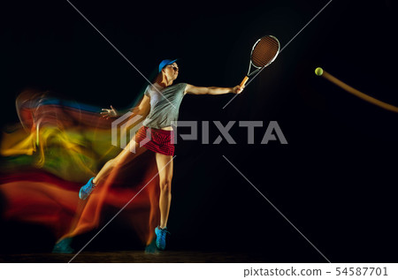 One caucasian woman playing tennis on black background in mixed light One caucasian woman playing tennis on black background in mixed light 54587701