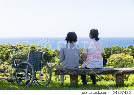 Senior and care helper taking a walk with a wheelchair Senior and care helper taking a walk with a wheelchair 54597420