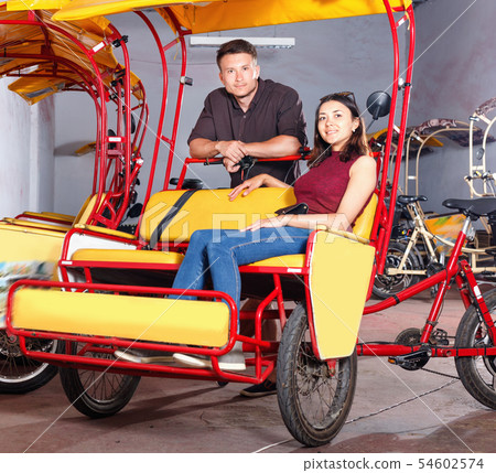 Cheerful girl with boyfriend wanting to hire touristic trishaw for urban trip Cheerful girl with boyfriend wanting to hire touristic trishaw for urban trip 54602574