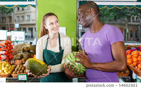 Smiling seller woman is helping man choose melone in the fruit market. 54602881