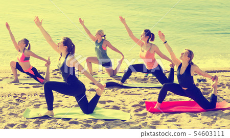 Group of sporty girls practicing various yoga positions during training on beach Group of sporty girls practicing various yoga positions during training on beach 54603111