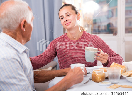 Mature man with daughter talking at table with cup of tea Mature man with daughter talking at table with cup of tea 54603411