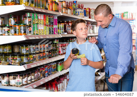 Happy family of father and teen son buying food products on shopping list in supermarket 54604087