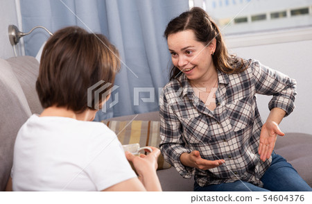 Smiling young female friends gossiping on sofa in home interior 54604376