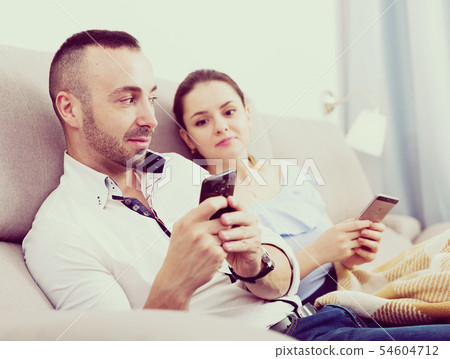 Couple is chatting on phone on the sofa Couple is chatting on phone on the sofa 54604712