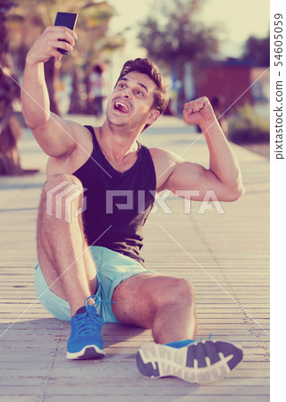 Cheerful sporty man showing biceps and taking selfie on beach fitness station Cheerful sporty man showing biceps and taking selfie on beach fitness station 54605059