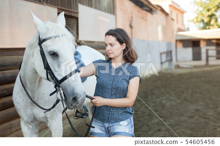 Mature smiling woman farmer standing with white horse at stable Mature smiling woman farmer standing with white horse at stable 54605456
