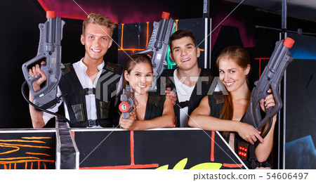 Group portrait of joyful young people with laser guns in their hands in room for playing laser tag Group portrait of joyful young people with laser guns in their hands in room for playing laser tag 54606497