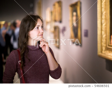 Woman attentively looking at paintings in art museum Woman attentively looking at paintings in art museum 54606501