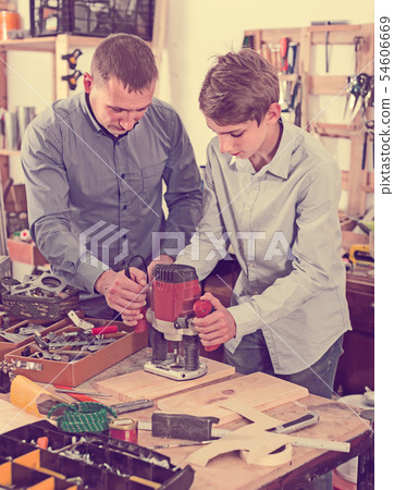 woodworker man and teenager with wood plank working in emerying machine at workshop 54606669