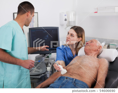 Woman and man doctors examines a senior man at abdomen 54606690
