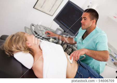 Man doctor examines a mature woman at abdomen with ultrasound 54606709