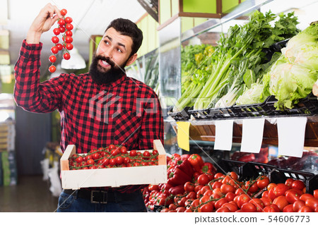 Man seller showing tomatoes in grocery shop Man seller showing tomatoes in grocery shop 54606773