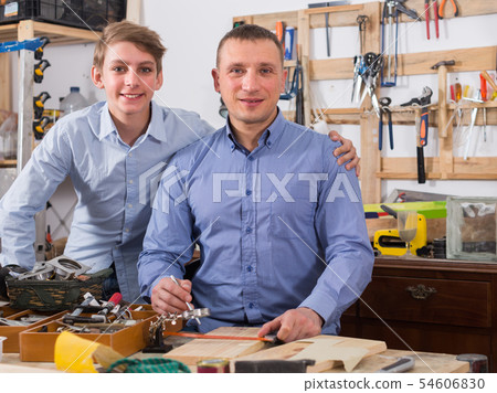 father and teen son working with wood plank in workshop father and teen son working with wood plank in workshop 54606830