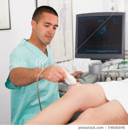 Man doctor during ultrasound test of young woman of knee Man doctor during ultrasound test of young woman of knee 54606846