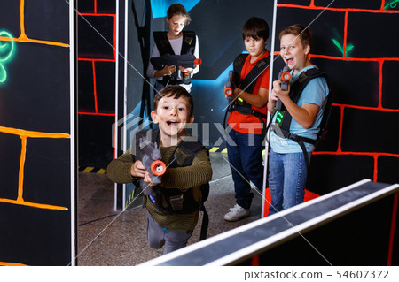 Emotional teen boy with laser pistol playing laser tag with friends on dark labyrinth Emotional teen boy with laser pistol playing laser tag with friends on dark labyrinth 54607372