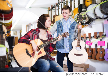 Teenagers examining guitars in shop 54607628