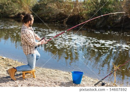 Adult man standing near river and pulling fish expressing emotions of dedication 54607892