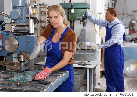 Female worker of glass factory drilling bores on machine 54608101