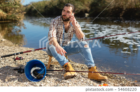 Adult fisherman talking on mobile phone by the river Adult fisherman talking on mobile phone by the river 54608220