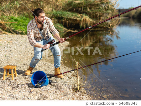 Happy fisherman pulls fish out of the river Happy fisherman pulls fish out of the river 54608343