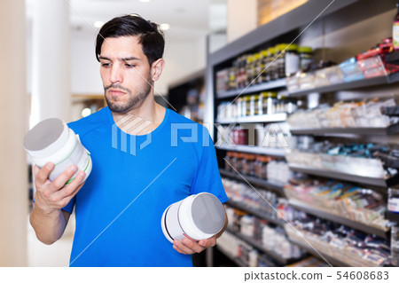 Serious young athletic man buying sport supplements in store Serious young athletic man buying sport supplements in store 54608683
