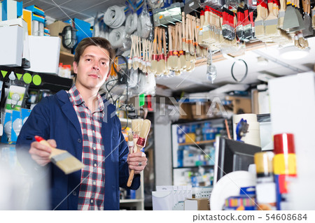 Worker man is standing near the counter and selling brushes Worker man is standing near the counter and selling brushes 54608684