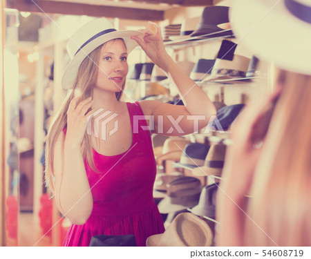 woman try on lady's hat and looking in mirror at outlet store 54608719
