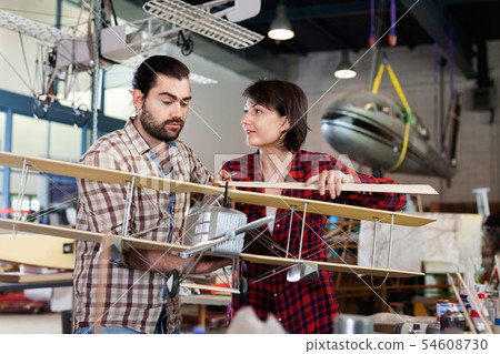 Positive couple enjoying their hobbies - modeling light airplanes in aircraft hangar Positive couple enjoying their hobbies - modeling light airplanes in aircraft hangar 54608730