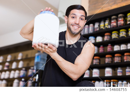 Attractive muscular man seller demonstration big pot of sport nutrition Attractive muscular man seller demonstration big pot of sport nutrition 54608755