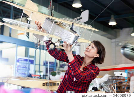 Smiling woman showing sports biplane model she created in aircraft workshop 54608979