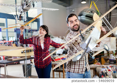 Cheerful team of aircraft enthusiasts holding sports airplane models in workshop Cheerful team of aircraft enthusiasts holding sports airplane models in workshop 54609059