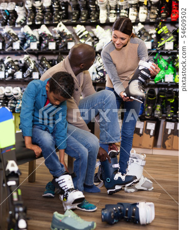 Young woman helping her husband and son choose new ski boots Young woman helping her husband and son choose new ski boots 54609502