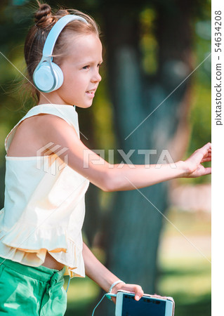 Little adorable girl listening music in the park Little adorable girl listening music in the park 54634208