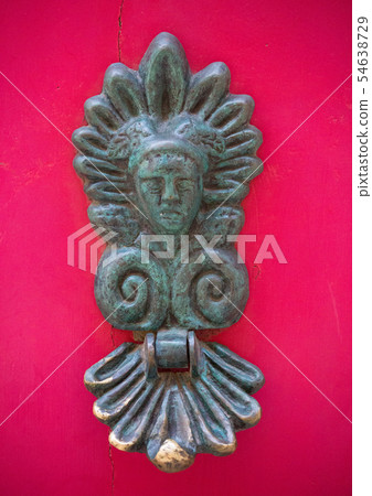 An old style decorative bronze door handle on a wooden red door, the distinctive feature and symbol An old style decorative bronze door handle on a wooden red door, the distinctive feature and symbol 54638729
