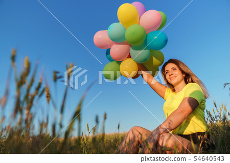 Young girl with colorful balloons in sunset meadow 54640543