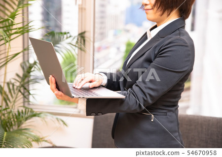 Woman in her thirties standing and typing on laptop-houseplant background Woman in her thirties standing and typing on laptop-houseplant background 54670958