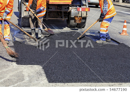 The working team smoothes hot asphalt with shovels The working team smoothes hot asphalt with shovels 54677190