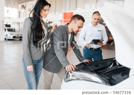 Manager shows the couple a new car in showroom 54677339