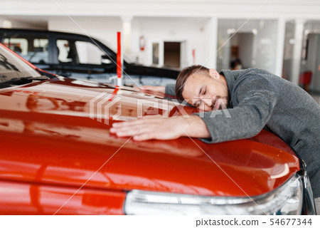 Man lying on the hood of new car in showroom Man lying on the hood of new car in showroom 54677344