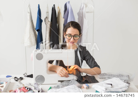 people, fashion and showroom concept - young fashion designer sews clothes on a sewing machine 54678745