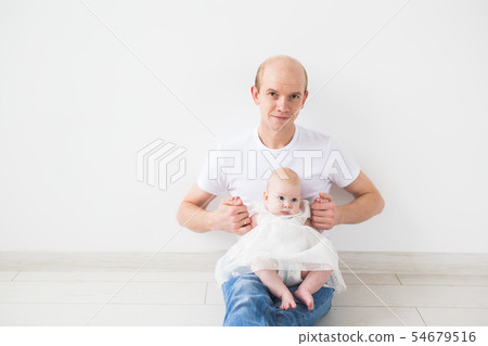 Infant baby, fatherhood and children concept - happy bald father with little daughter on his knees 54679516