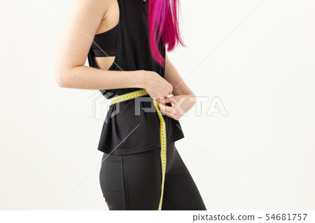 Unidentified young girl hipster with purple hair measures her waist with a measuring tape on a white Unidentified young girl hipster with purple hair measures her waist with a measuring tape on a white 54681757