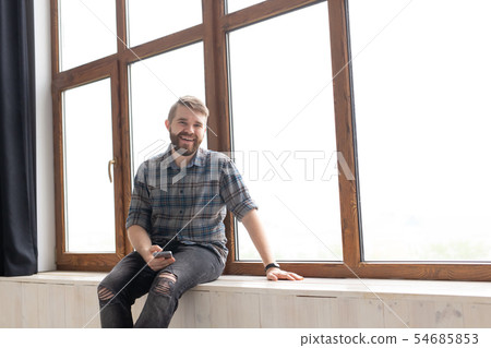 Cute young hipster guy with stylish clothes is sitting on social networks using a smartphone and 54685853