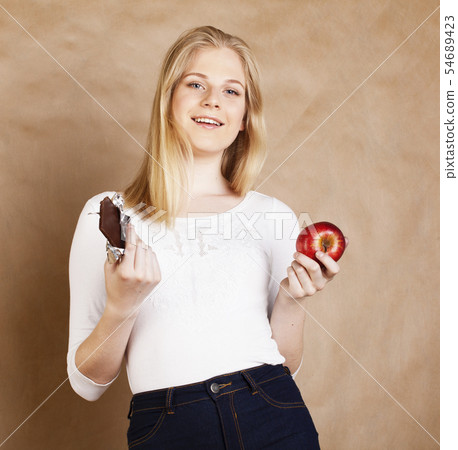 young beauty blond teenage girl eating chocolate smiling, choice between sweet and apple 54689423