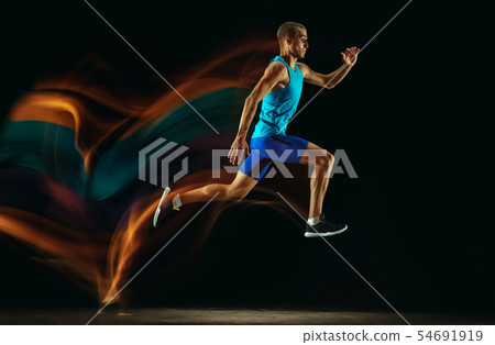 Professional male runner training isolated on black studio background in mixed light Professional male runner training isolated on black studio background in mixed light 54691919